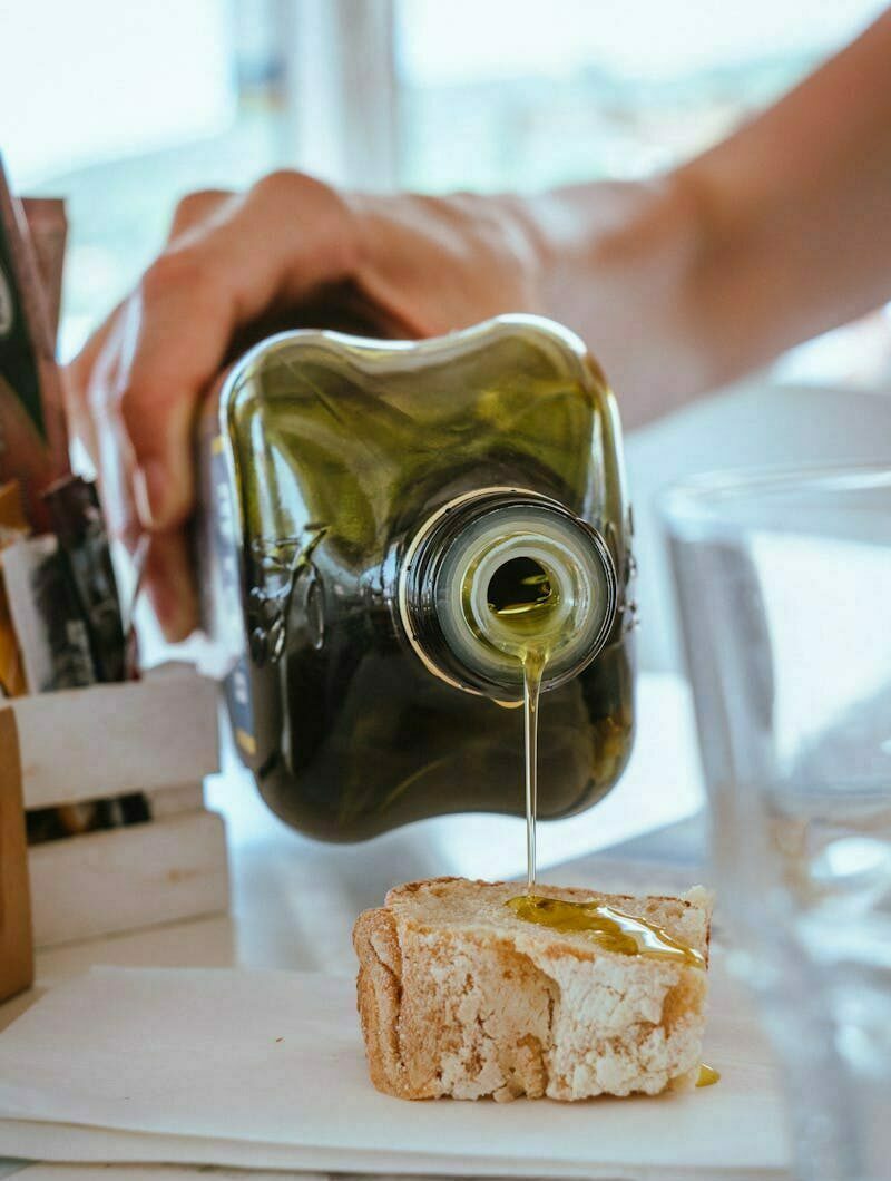 Close-up of olive oil being poured on a slice of bread, emphasizing texture and flavor.